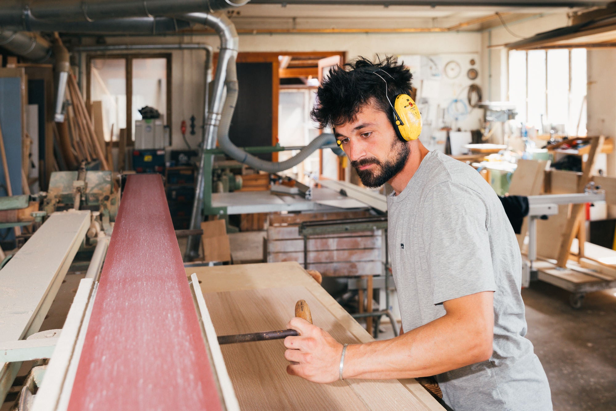 Ein Schreiner arbeitet konzentriert an einer großen Schleifmaschine mit rotem Schleifpapier. In der hellen, professionellen Werkstatt wird Massivholz für ein Möbelstück geschliffen.