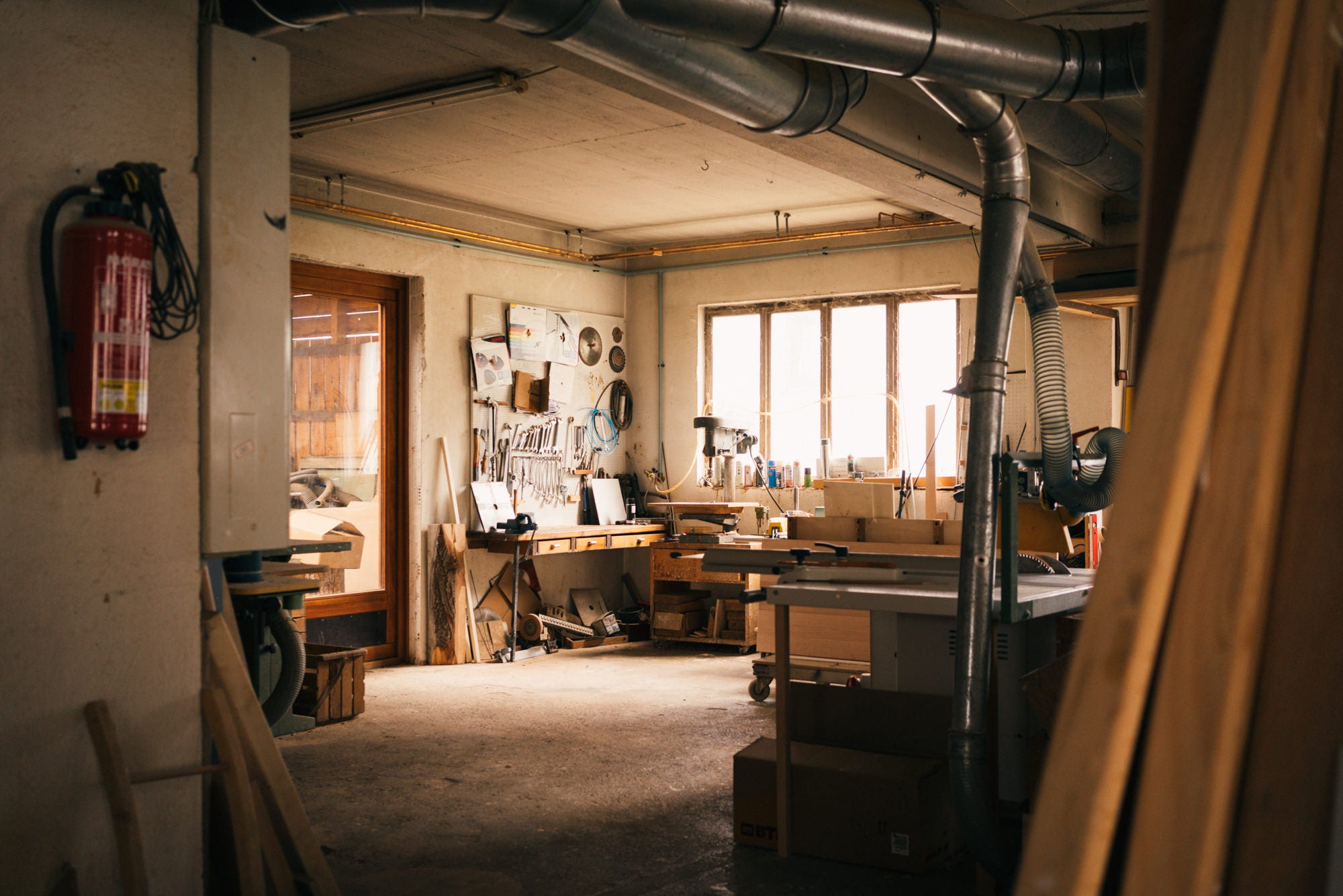 Professionelle Schreinerei-Werkstatt, in der Massivholz verarbeitet wird. Das Bild zeigt eine Formatkreissäge und andere Werkzeuge in einer warmen gemütlichen , aufgeräumten Umgebung.