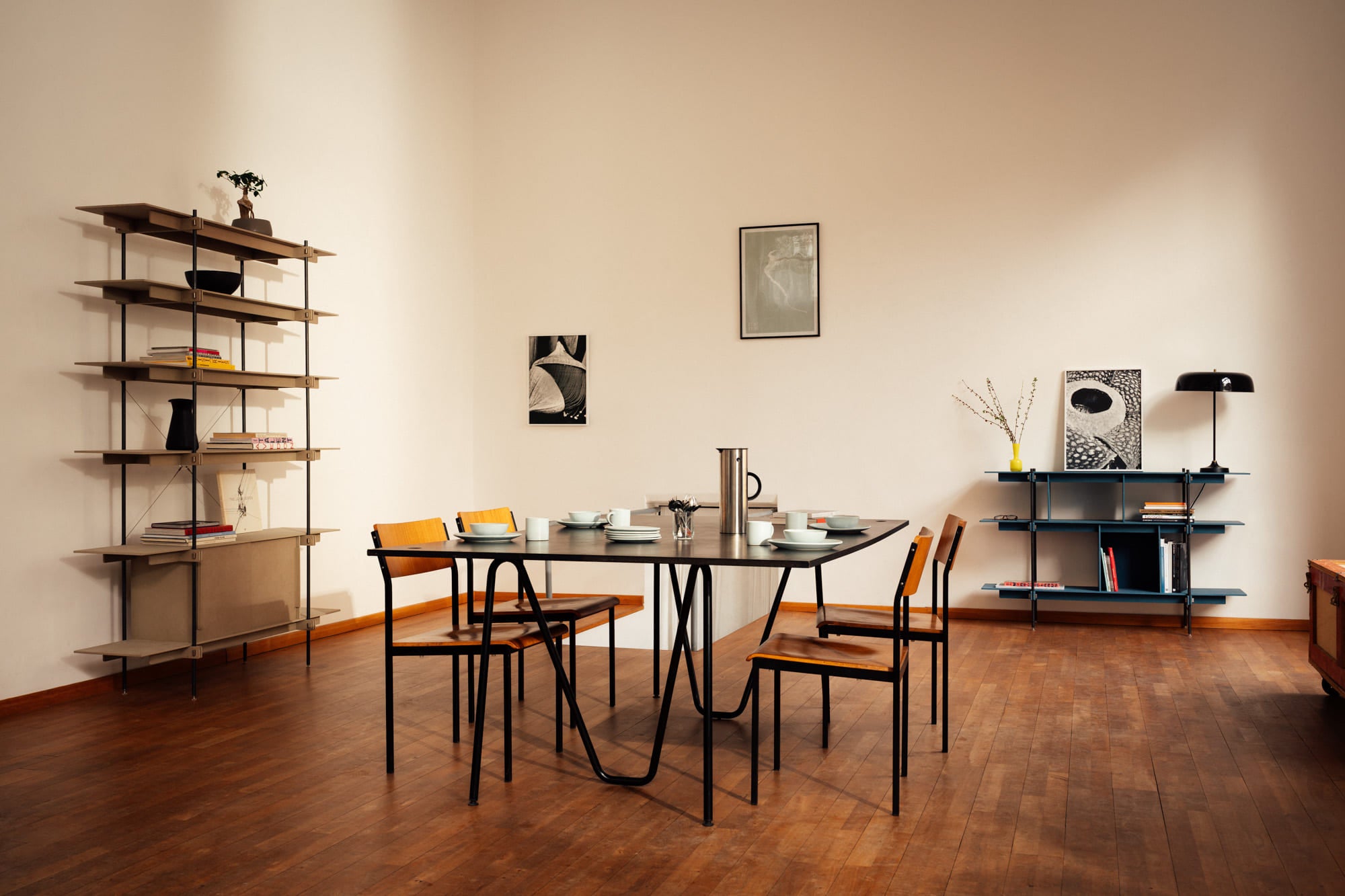 Zwei Design-Regale vom "TIGHT"-Regalsystem von Holzfabrikat in einer hellen, schicken Wohnung. Der moderne, schwarze Tisch im Mittelpunkt ist stilvoll gedeckt und passt perfekt zu den Möbeln.