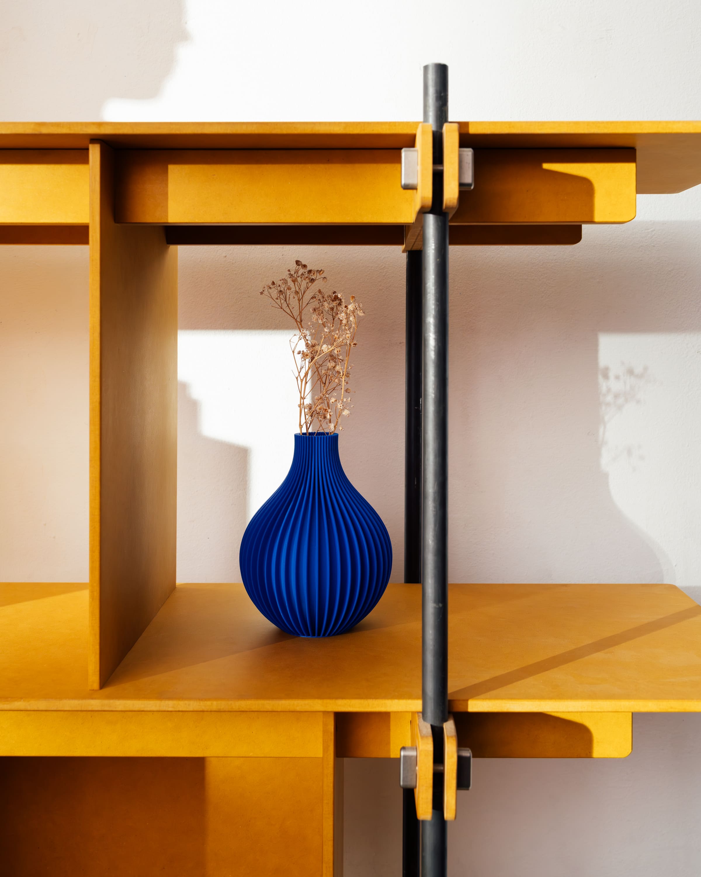 Modernes Regalsystem aus hellem Holz mit schwarzem Stahlrahmen und offenem Fach mit blauer Vase.