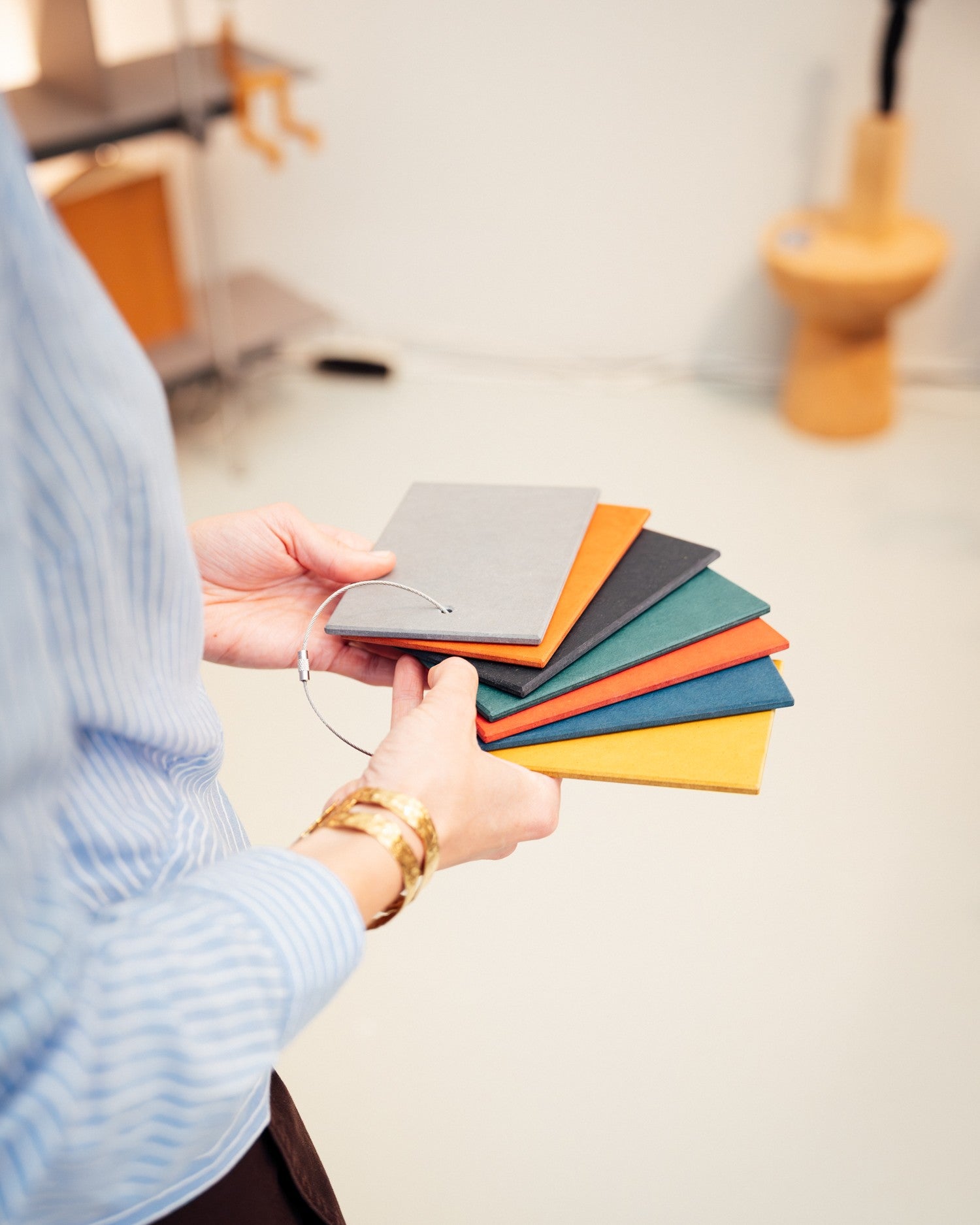 Hand hält Farbmuster mit sechs rechteckigen Holzplatten in Grau, Orange, Blau, Grün, Rot und Gelb.
