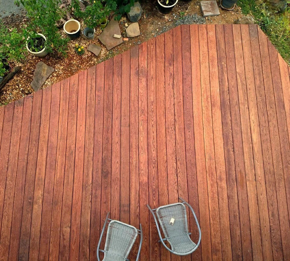 Terrasse aus Holz mit warmen Holzdielen, dazu zwei graue Stühle, angrenzender Holz Balkon mit Pflanzen, Terrasse Ideen.