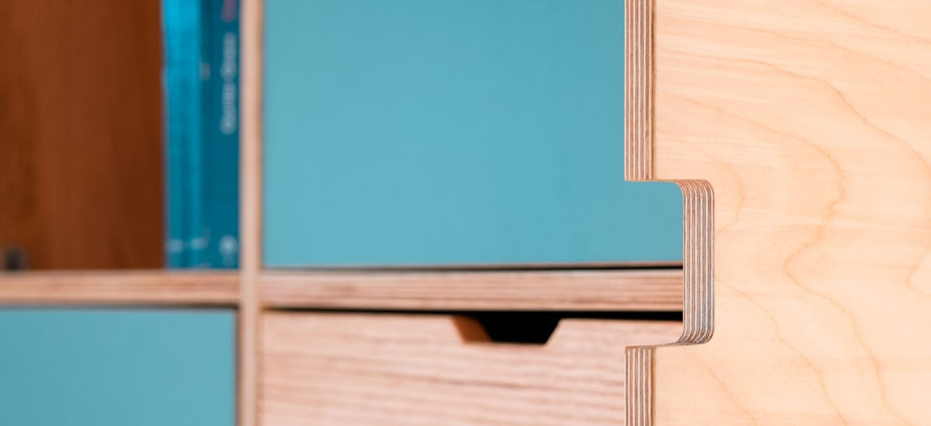 Detailaufnahme einer gefrästen Griffmulde an einem Einbauschrank. Die Kante zeigt die Schichtstruktur der Birke Multiplex Platte, während die Oberfläche  der türen mit einer türkisfarbenen HPL-Beschichtung versehen ist.