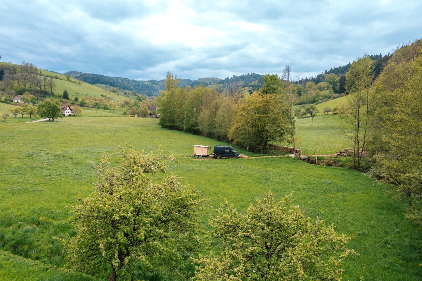 Drohnenaufnahme einer mobilen Sauna auf Anhänger, die auf einer grünen Wiese im Schwarzwald steht. Die Aufnahme bietet einen Überblick über das naturnahe Konzept für alle, die eine mobile Sauna kaufen möchten.
