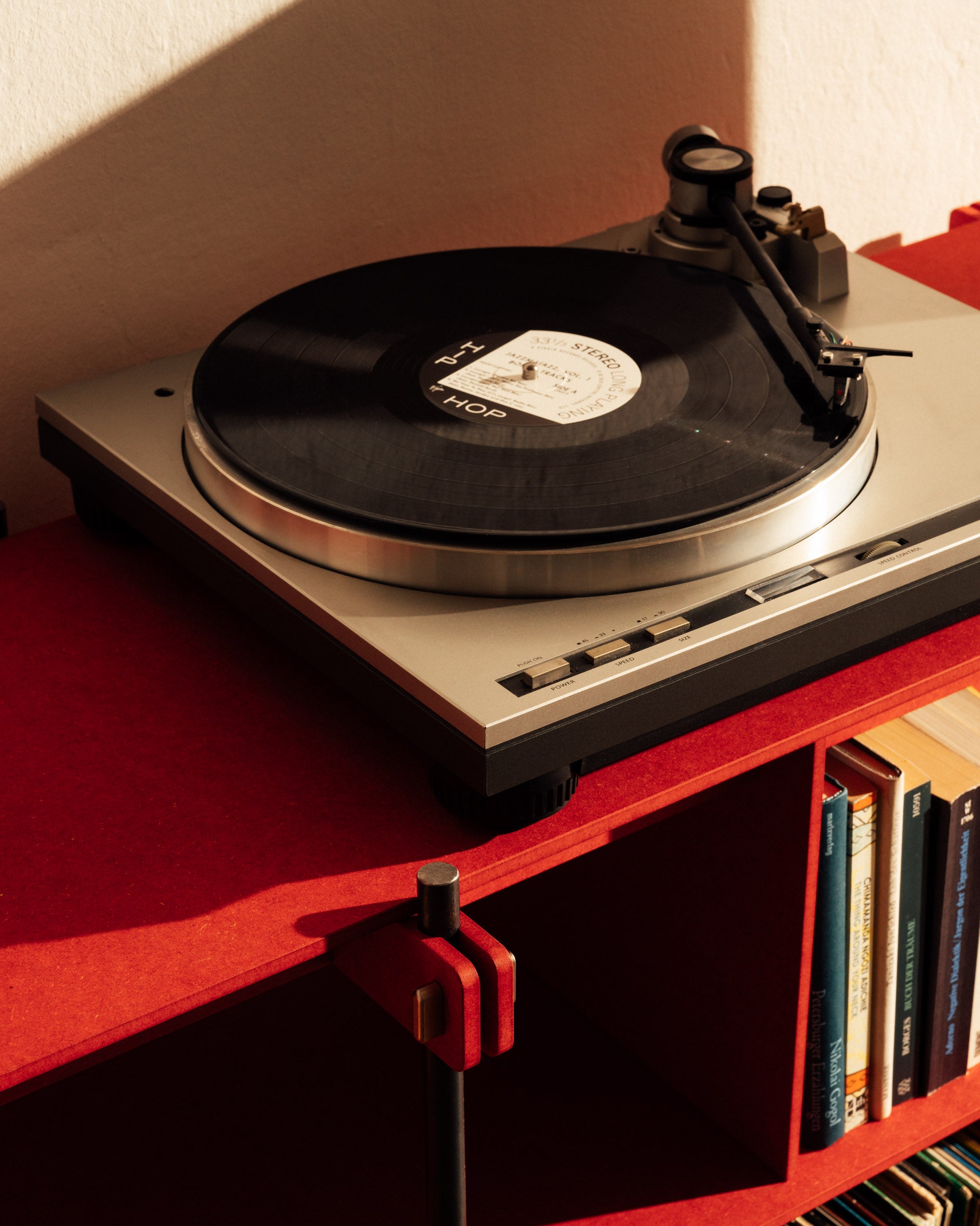 Rotes Design Regal mit Stahlrahmen, offenes Regal mit Büchern und Plattenspieler oben.