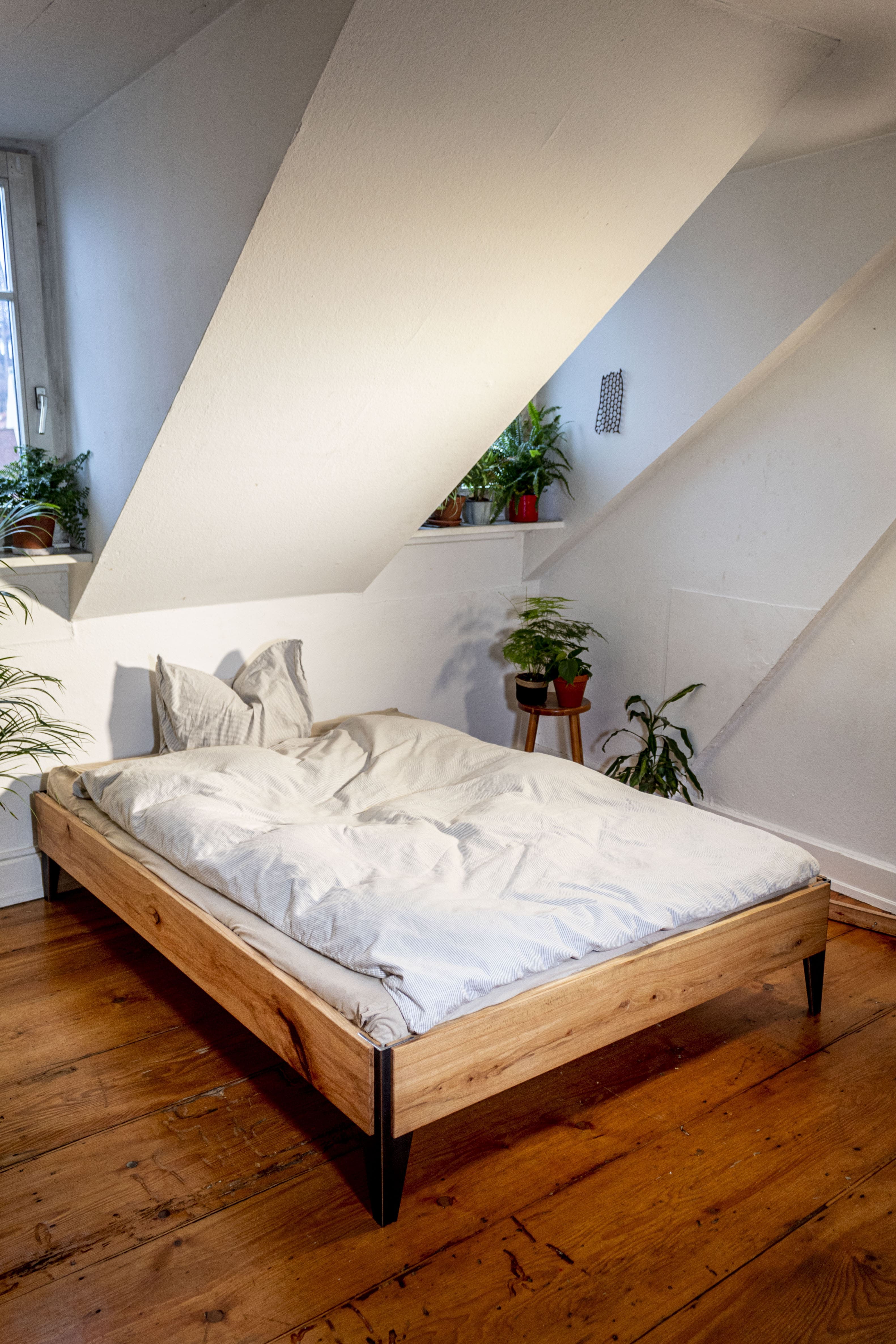 Schlafzimmer mit schlichtem Bettgestell aus Holz und schwarzem Stahl, minimalistisches Regalsystem Design am Fenster.