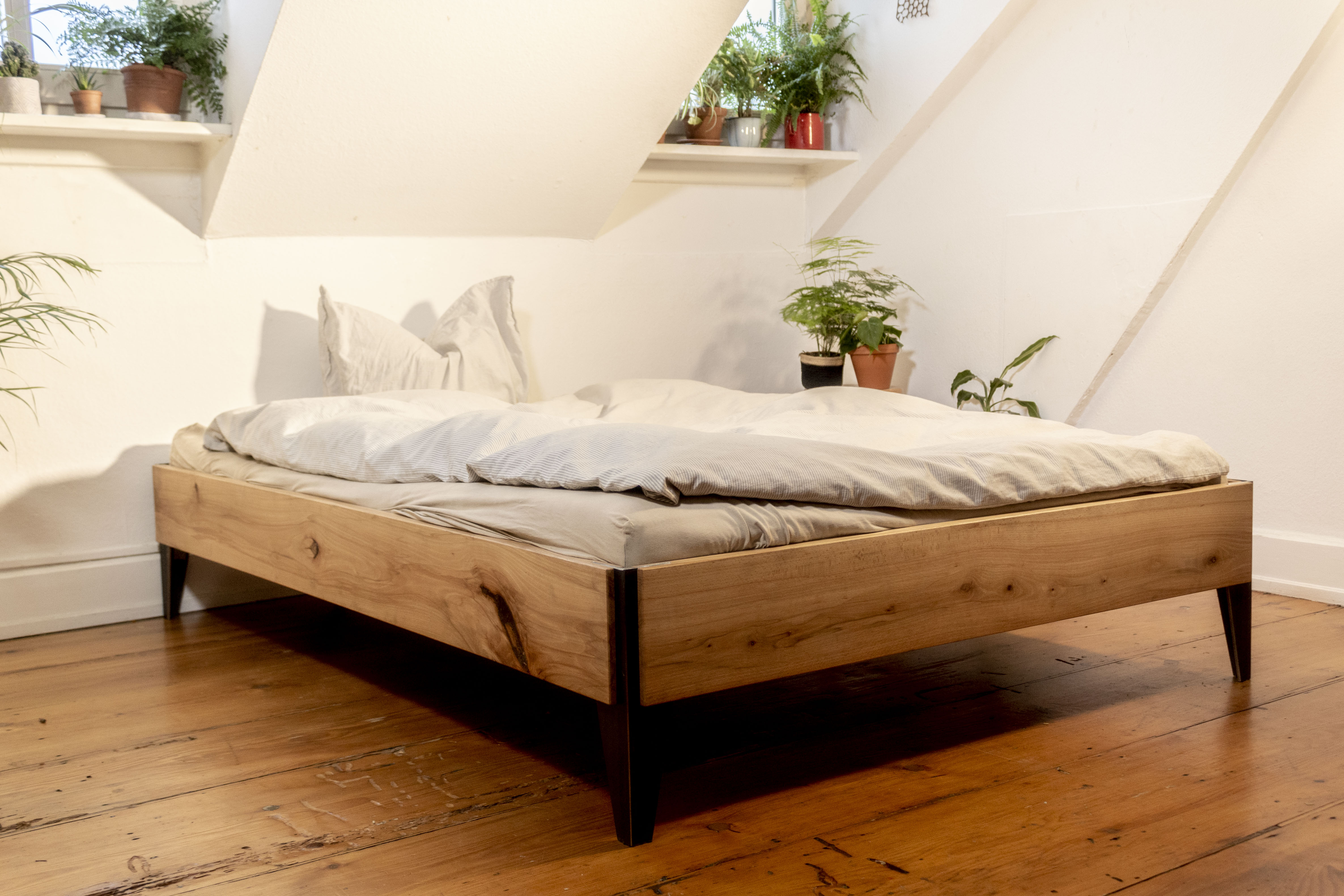 Gemütliches Schlafzimmer mit vielen Pflanzen und einem Bettgestell aus Holz und Stahl. Das minimalistische bett passt zum einrichtungsstil