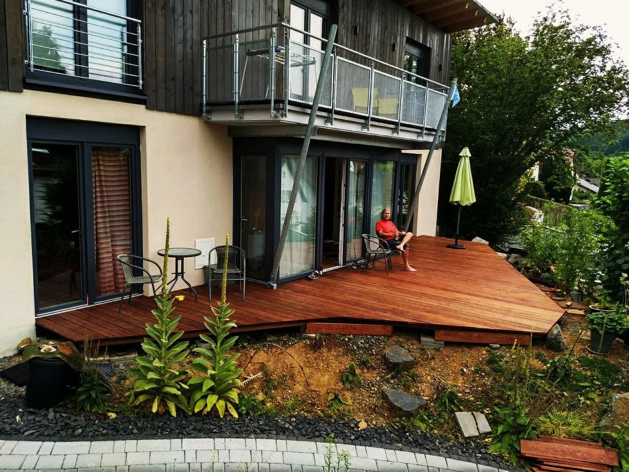 Terrasse aus Holz mit dunkelbrauner Holzterrasse und modernem Metall Balkon am Haus.