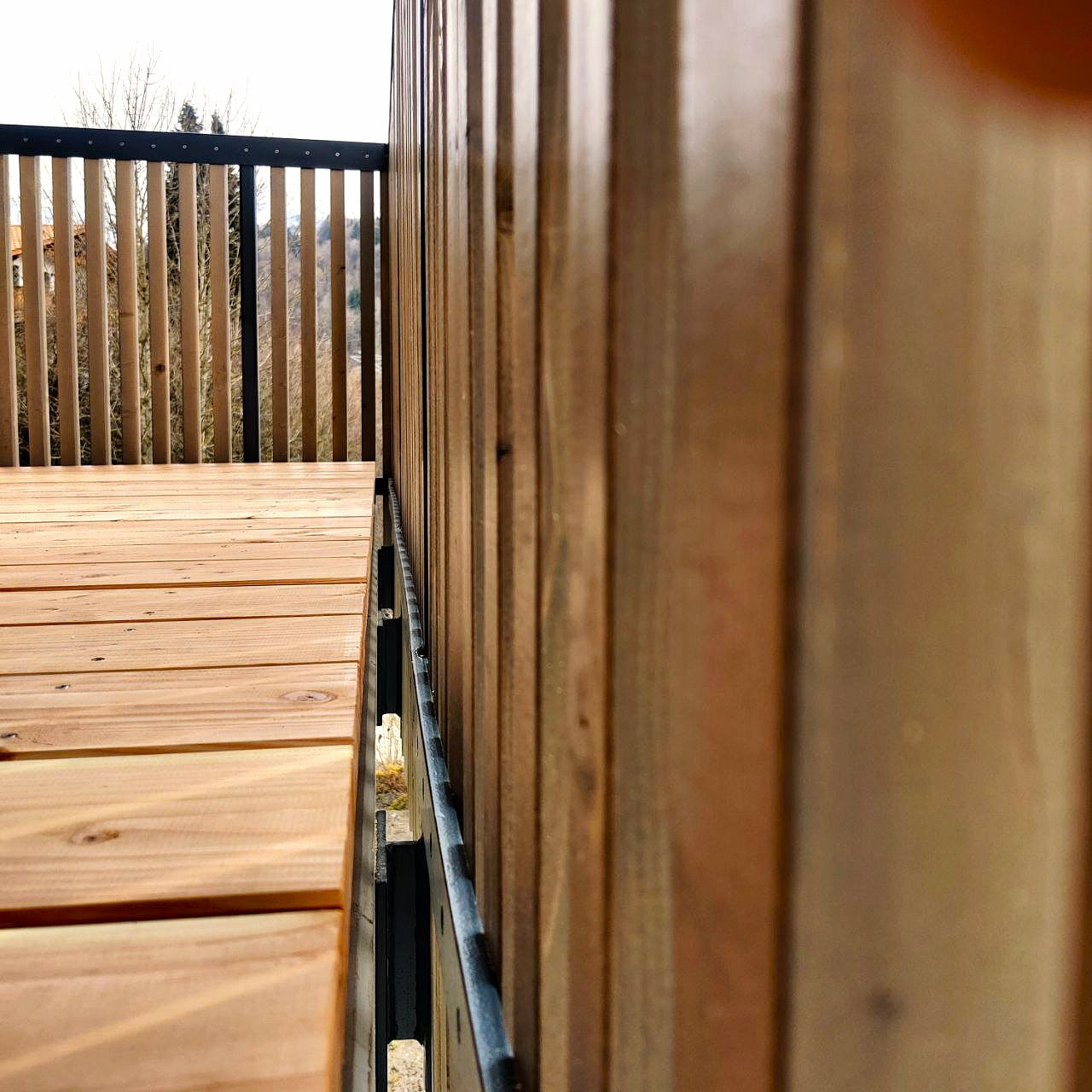 Eine präzise gefertigte Holzterrasse mit einem Holzgeländer und einem modernen Metallbalkon. Die ökologisch behandelte Oberfläche aus regionalem Douglasienholz ist ein stilvolles Beispiel für moderne Terrassenideen.