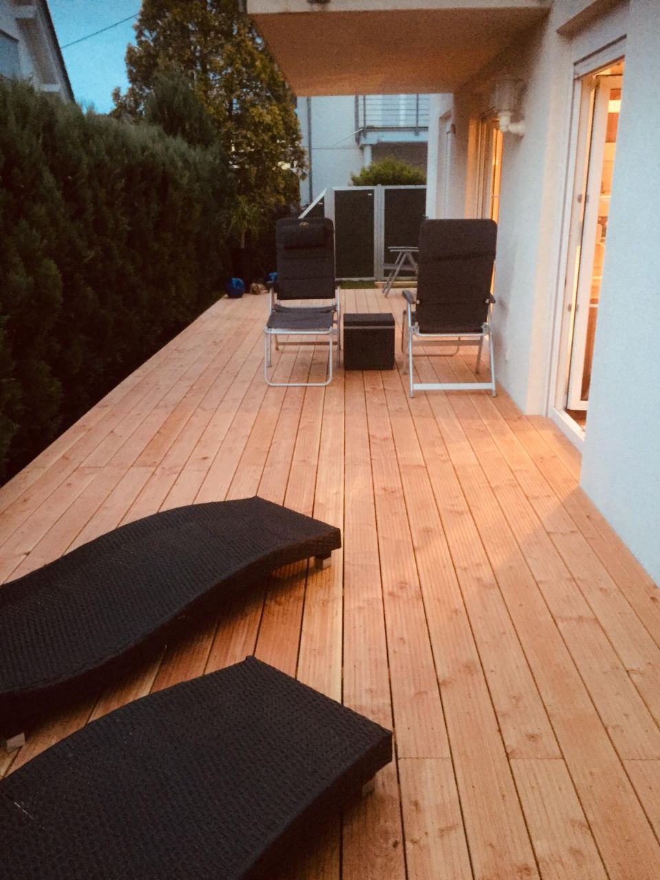 Terrasse aus Holz mit zwei schwarzen Liegestühlen und Holz Balkon am modernen Balkon mit Metall Geländer.