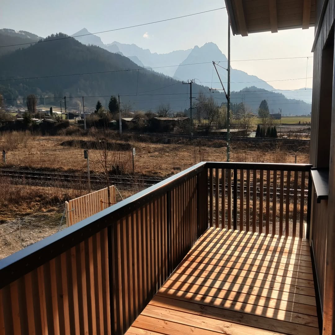 Holz Terrasse mit senkrechten Latten, sonnig, umgeben von Bergen, Terrasse aus Holz und Holz Balkon mit Metallgeländer.
