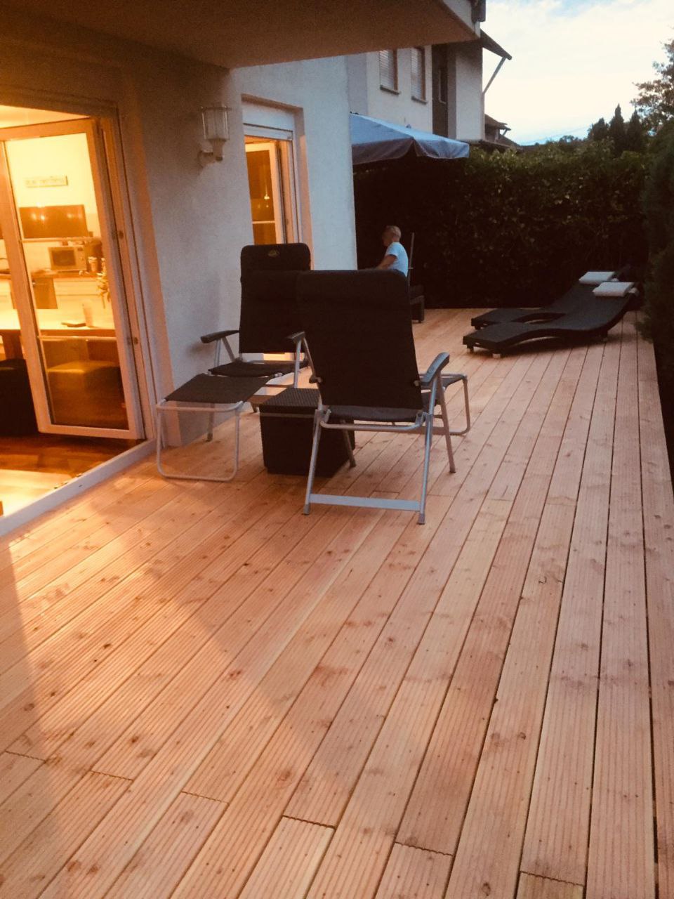 Terrasse aus Holz mit Holzboden, Gartenmöbeln und Blick auf Holzbalkon, Abendlicht.