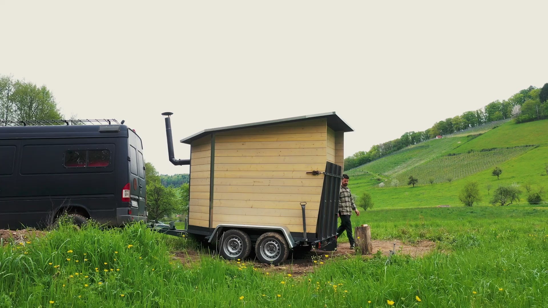 Video mit Drohnenaufnahmen einer mobilen Sauna aus Holz. Das Video zeigt das kompakte Design mit Ofen, ideal für die Landschaft im Schwarzwald oder in der Nähe von Freiburg.